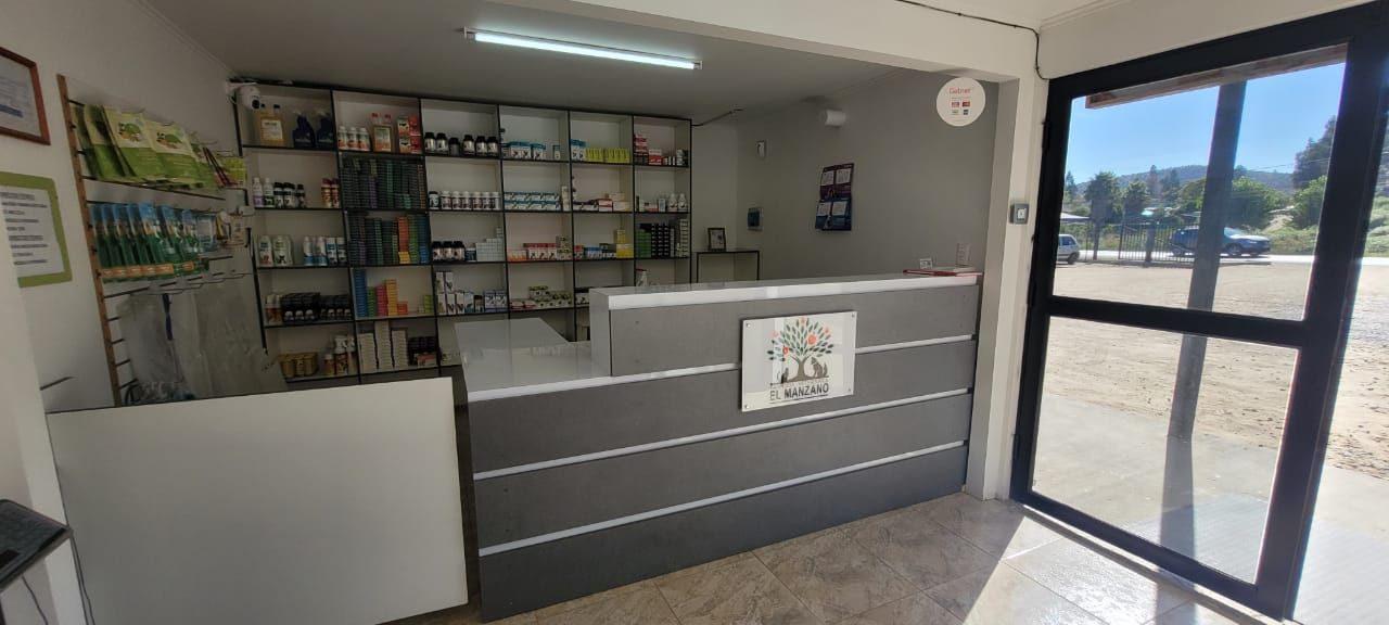 Mesón de la farmacia con la puerta abierta hacia el estacionamiento y los cerros